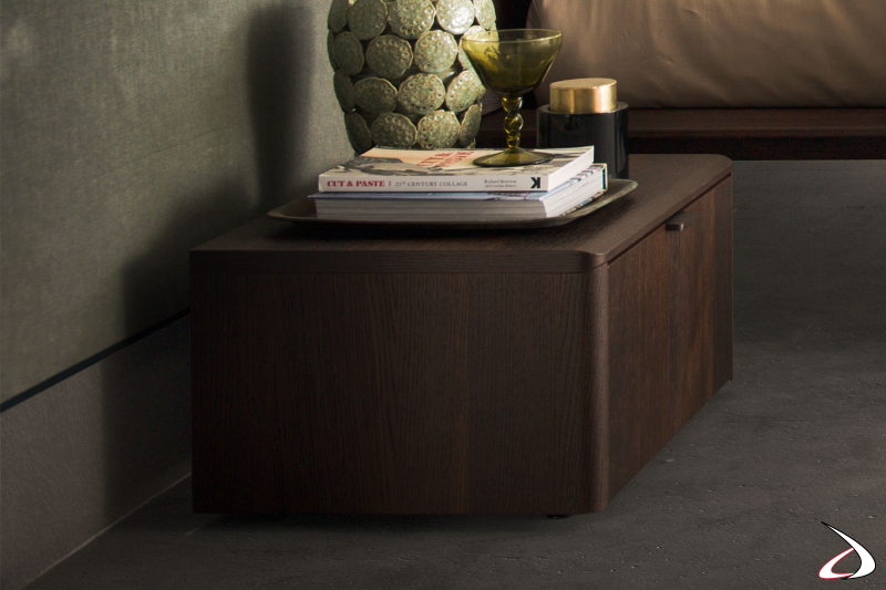 Nachttisch mit Füßen mit eleganten Linien, geformte externe Elemente, die eine rechteckige Schublade mit Metallgriffen umgeben.
