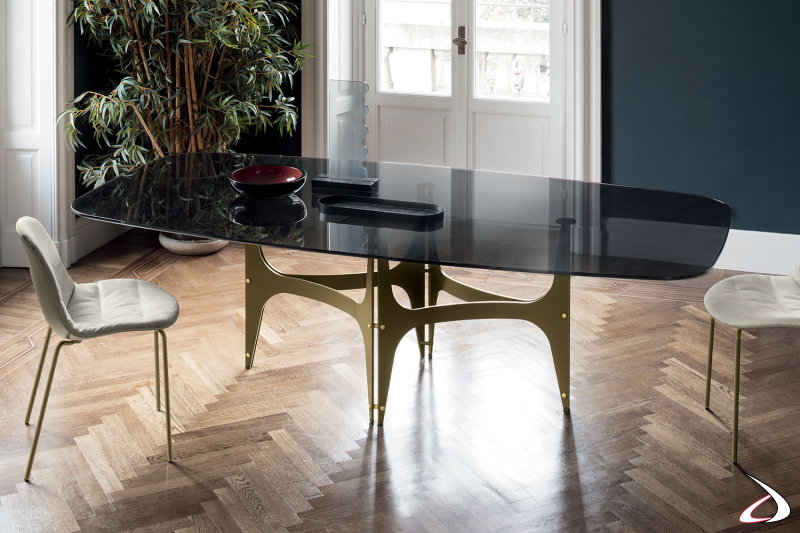 Tavolo di design da soggiorno con piano a botte in cristallo fumè trasparente e basamento centrale ad archi in color oro