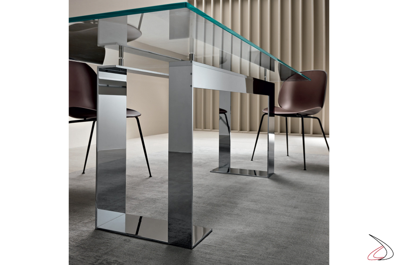 Tavolo moderno con top in vetro, caratterizzato da un particolare basamento in metallo dal design asimmetrico.