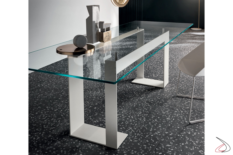 Tavolo moderno ed elegante in vetro, caratterizzato da una struttura di design in metallo verniciato bianco opaco.