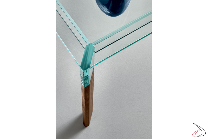 Tavolo moderno dal design minimalista che si caratterizza per il particolato top in vetro poggiato su gambe in noce canaletto sbontabili.