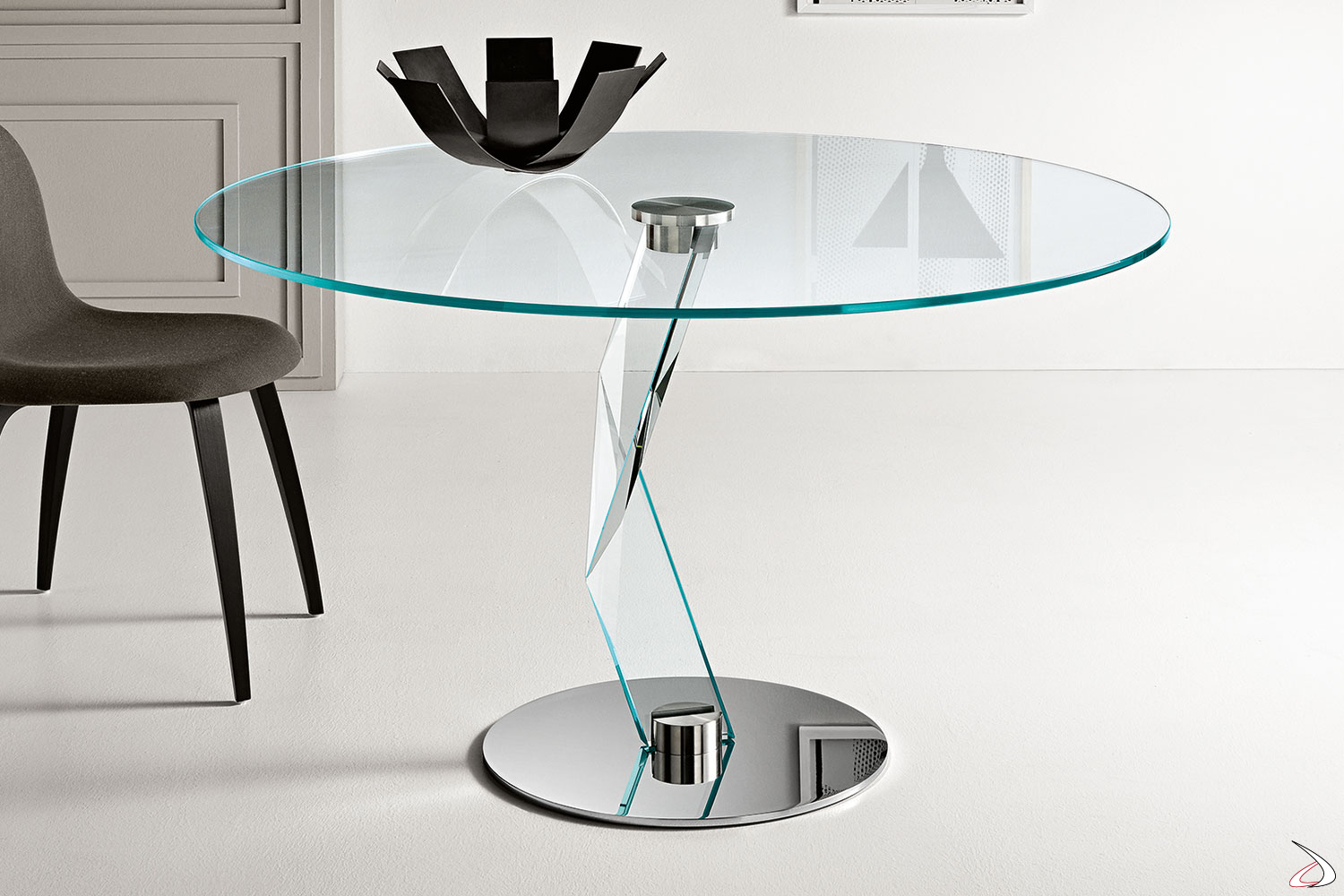 Tavolo moderno ed elegante in vetro temperato con top rotondo, caratterizzato dalla forma scultorea della gamba portante e dalla base in metallo cromato che permettono giochi di luce.